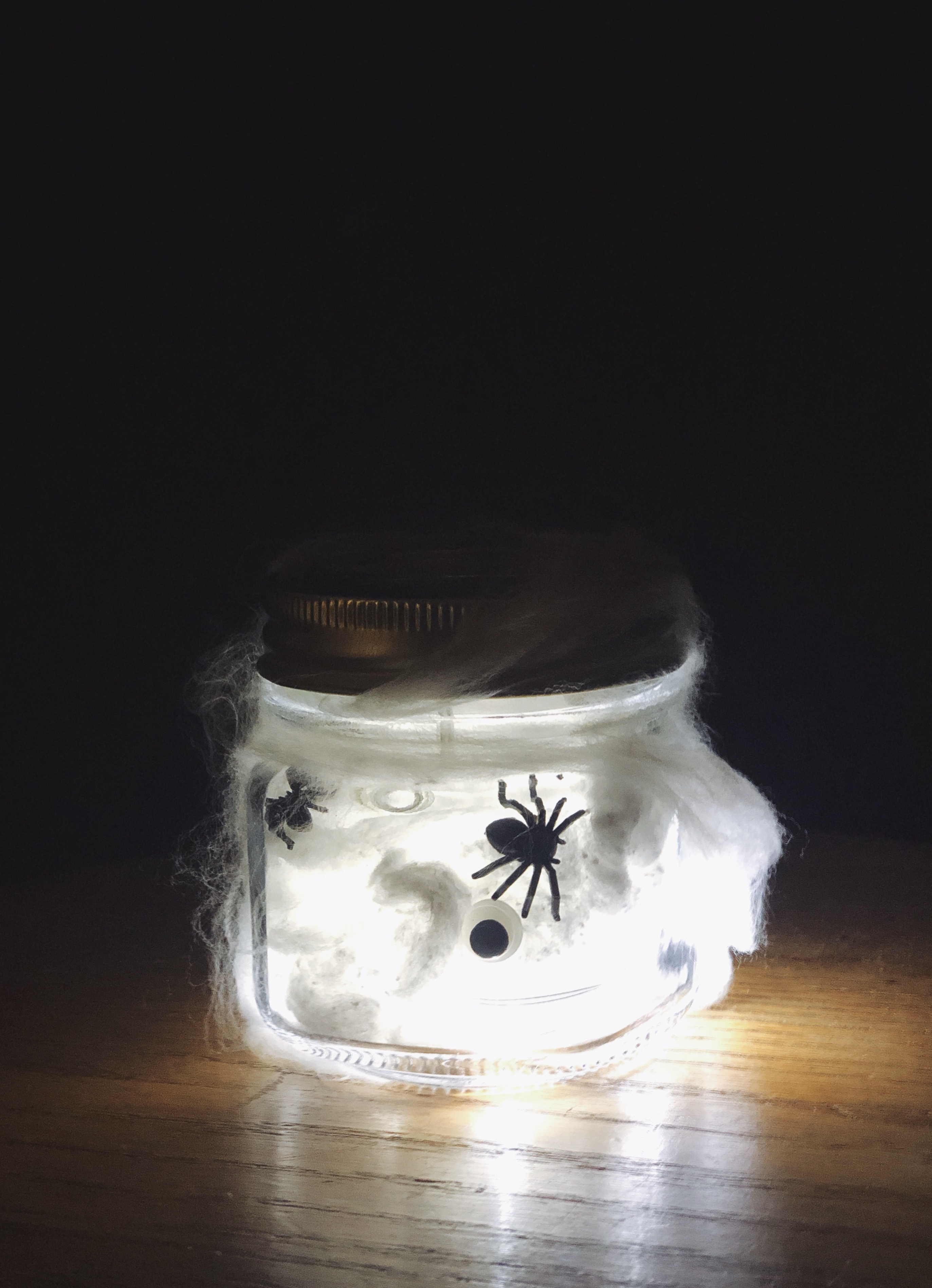 Picture of a spooky nightlight, a jar filled with fairy lights, spiders, googly eyes, and cotton spider webs.
