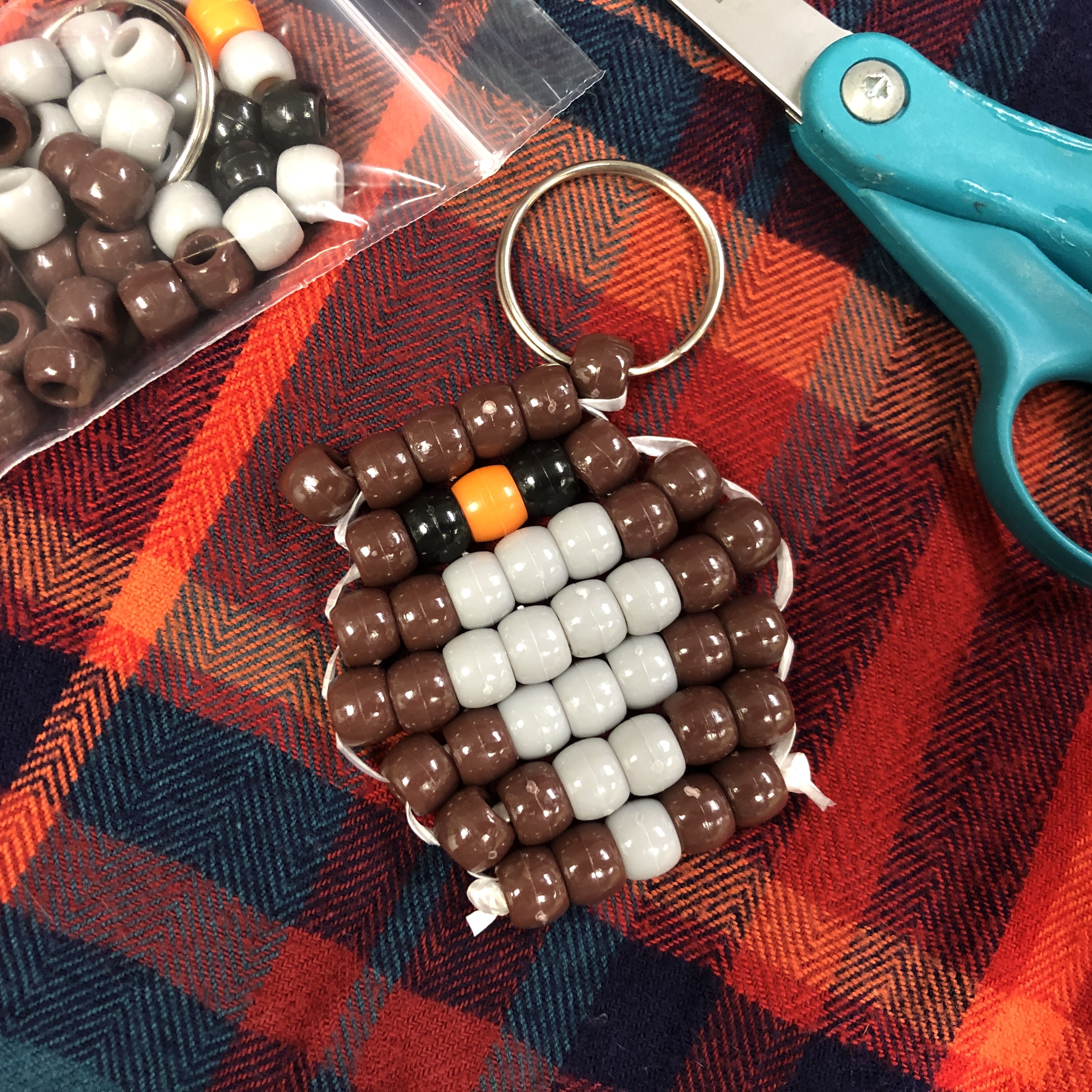 Image of beaded owl on plaid blanket with bag of beads and scissors nearby.
