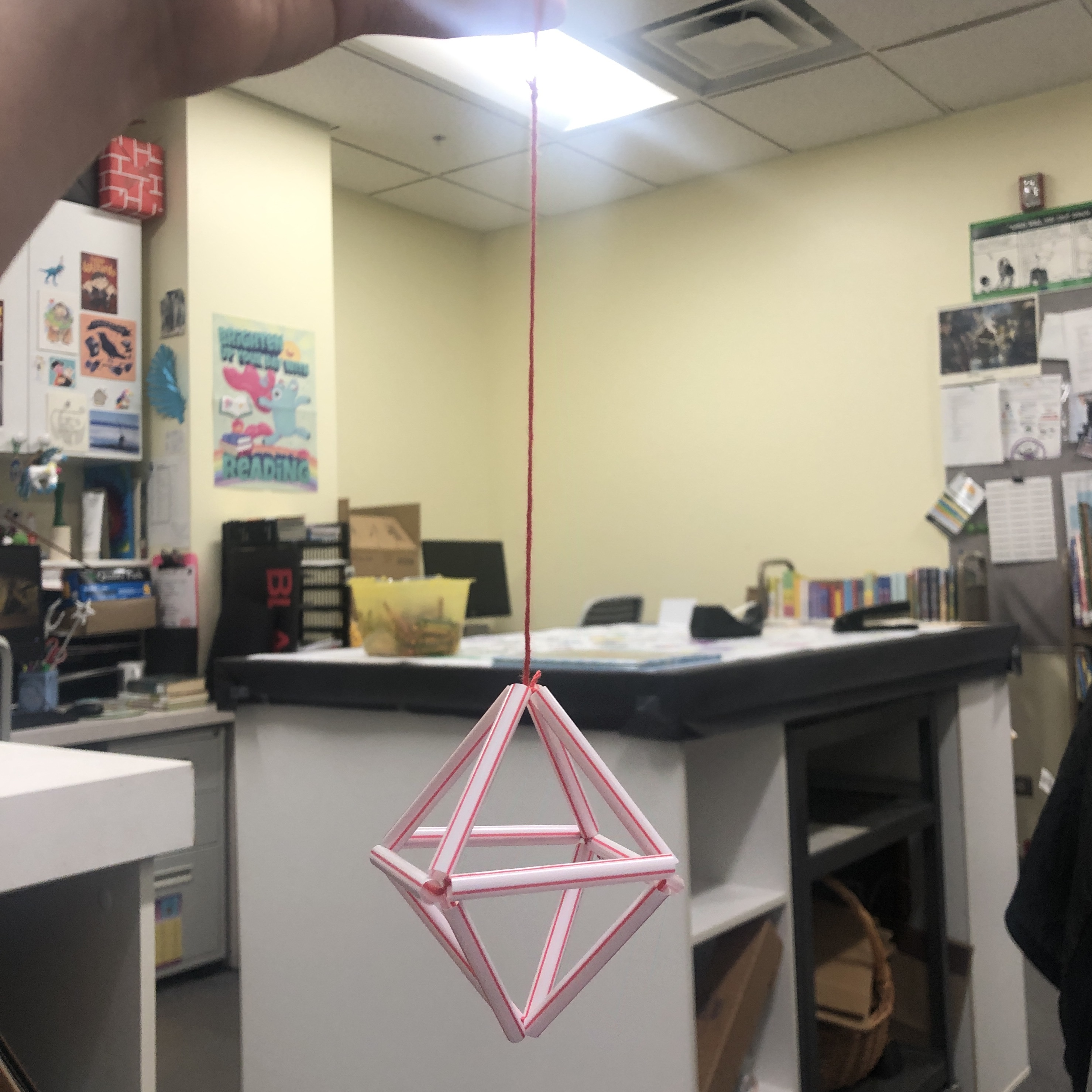 Photo of a hanging geometric diamond shape made out of straws and string.