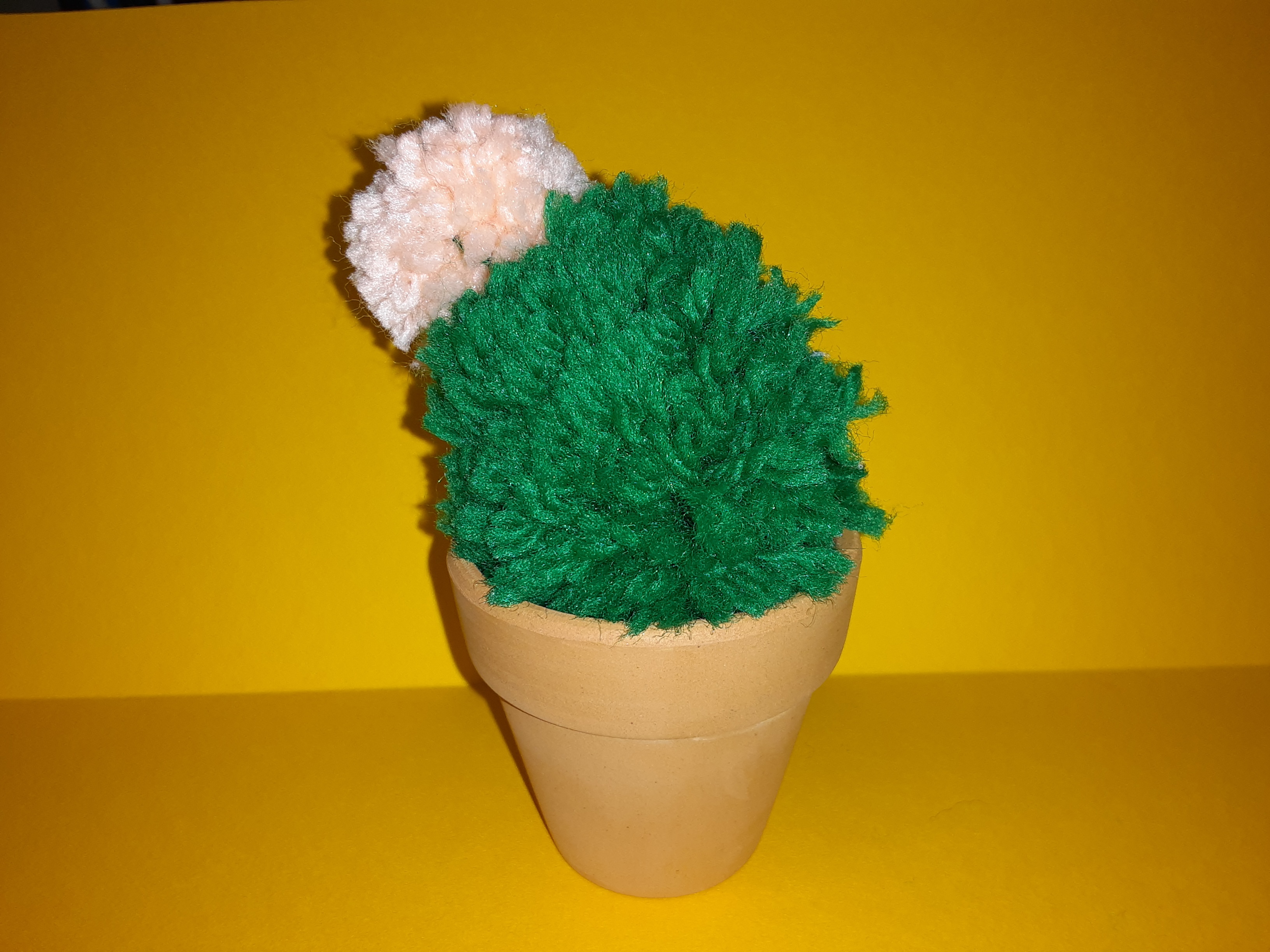 A small flowering cactus made of yarn in a 2" clay pot