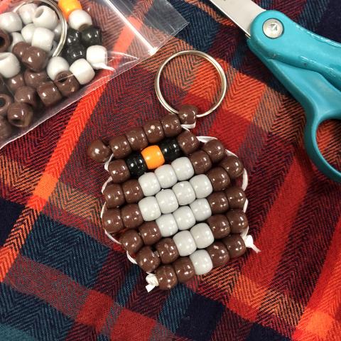 Image of beaded owl on plaid blanket with bag of beads and scissors nearby.